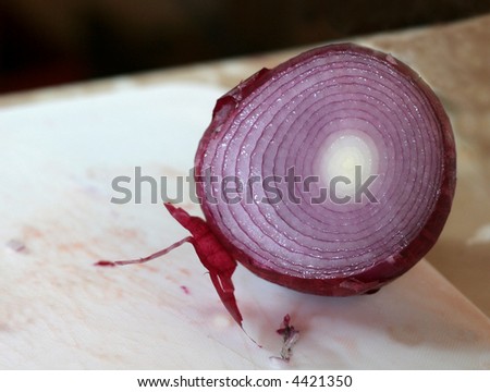 A red (spanish) onion freshly cut sitting on cutting board.