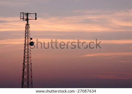 The silhouette of a cell phone tower shot against the orange cast of the setting sun.