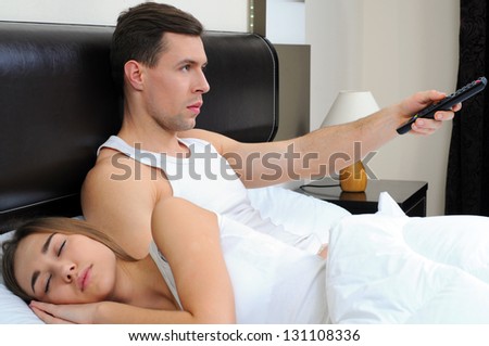 man watches television and his wife sleeps