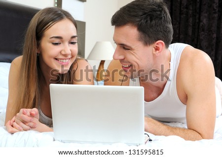 Happy couple with laptop in bed watching fun movie on computer in bed before sleeping.