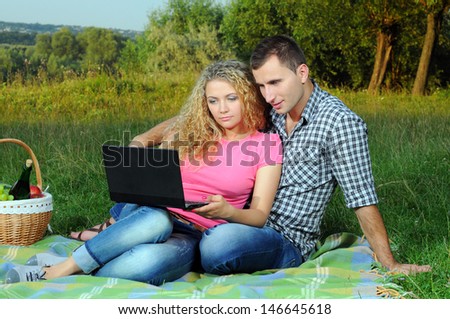Happy couple on picnic with the laptop in wood