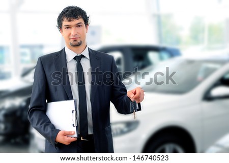 Handsome young classic car salesman standing at the dealership holding a key for a car