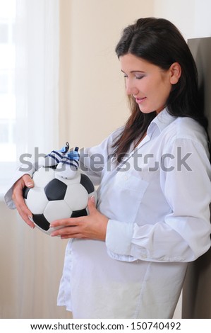 young pregnant woman with a soccer ball and athletic shoes for baby. waiting for the boy