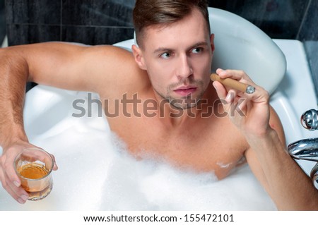 young man taking a bath, drinking whiskey and smoking cigar