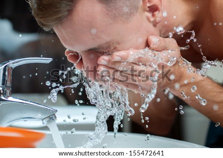 Bright Caucasian Man Spraying Water On His Face After Shaving In The Bathroom At Home