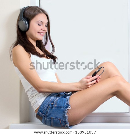 Listening to the music. Beautiful young woman listening to the music while sitting on the windowsill
