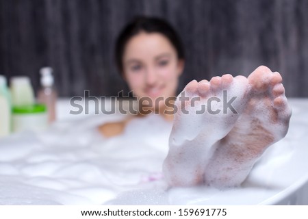 Beautiful smile woman washing leg with pink sponge in bath with foam, young girl bathing in bathtub, relaxing in bath jacuzzi
