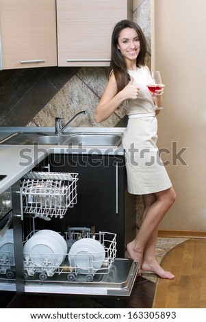 Kitchen Woman. Girl in the kitchen using dishwasher. view of young woman in kitchen doing housework.  drinking wine