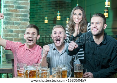 Three men and one girl with beer rejoice the victory of their favorite team in the pub