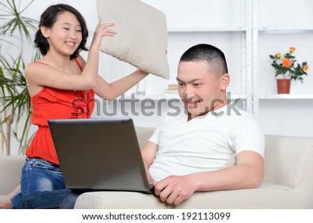 Portrait of young Asian couple sitting on sofa at home, using laptop computer, smiling.
