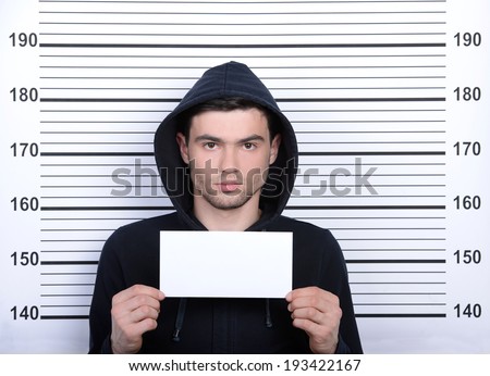 Busted burglar. Angry burglar holding a white poster while standing against police line-up