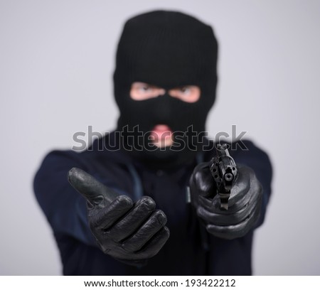 Masked robber with gun aiming into the camera against a black background