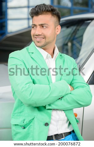 Portrait of young Indian business man, standing near a car on a background of the business building