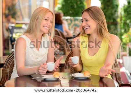 Two friends talking and drinking coffee, sitting in a cafe outdoors