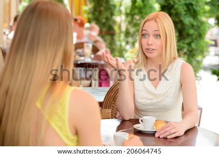 Two friends talking and drinking coffee, sitting in a cafe outdoors