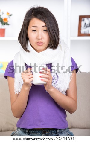 Pretty asian woman is sick. She is drinking hot tea at home.