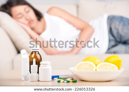 On the table are medicines and lemons. In the background is the asian woman on the bed.