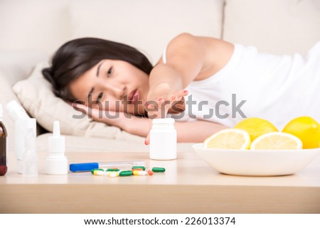 Asian woman is sick. She needs medication. Medicine are on the table.