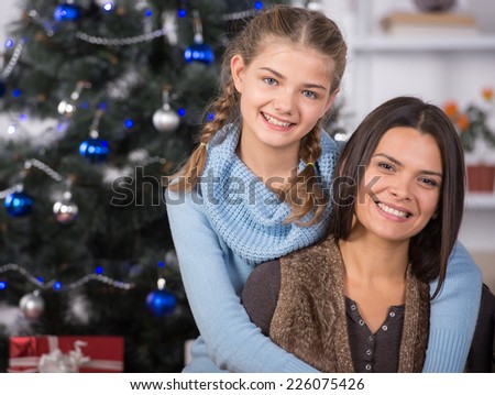 Smiling mother and daughter in christmas time. Christmas tree and gifts in background.