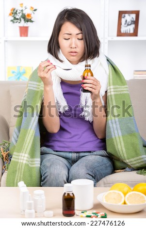 Young asian woman treats colds. She is taking medications. Medicines and lemons on the table. She has headache.
