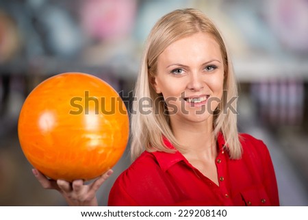 Beautiful young woman in a bowling alley with ball, is smiling and looking at the camera.