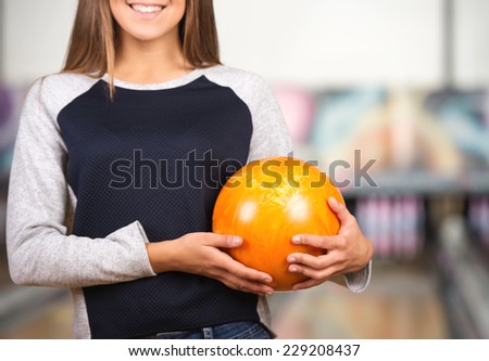 Smiling young woman in a bowling alley is holding red ball.