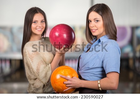 Two smiling women with balls in bowling club are looking at the camera.