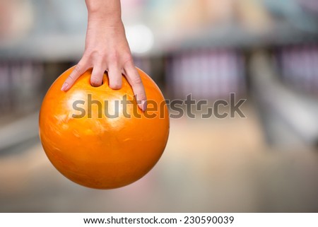 Close-up hand of woman is holding ball against bowling alley.