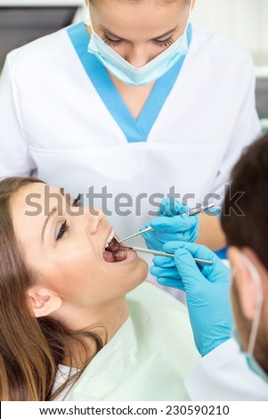 Close-up of female dentist is examining pretty female patient\'s mouth in clinic.
