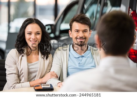 Some paperwork before buying a car. Young car salesman talking to a couple in auto salon.