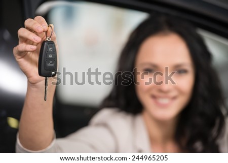Happy young woman is holding keys to new car and looking at the camera. Focus on keys.