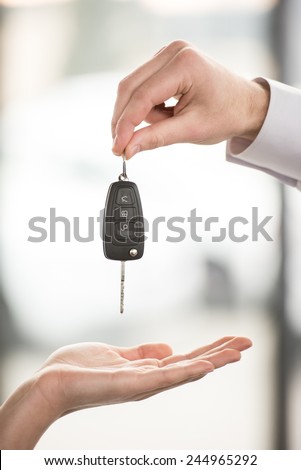 Car dealer is giving keys to a customer in a car shop. Close-up.