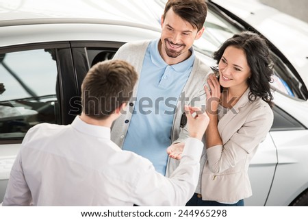 Car salesman is giving the key of the new car to the young attractive owners.