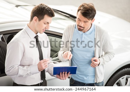 Car salesperson demonstrating a new automobile to young couple.