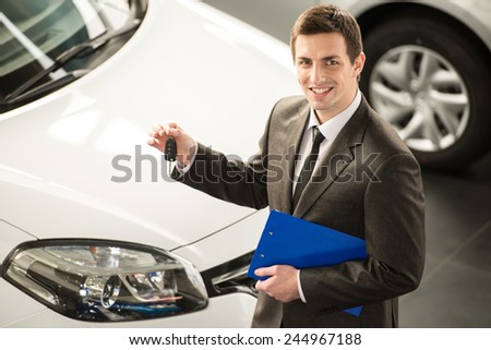 Young man consultant in showroom is standing near car. Top view.