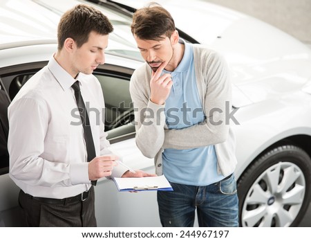 Car salesperson demonstrating a new automobile to young couple.