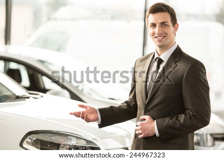 Young man consultant in showroom is standing near car. Top view.
