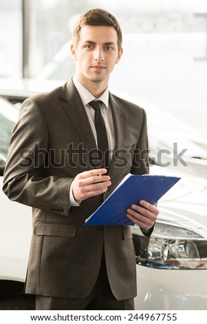 Young man consultant in showroom is standing near car.