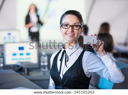 Young smiling business woman is holding a discount card while sitting in modern conference hall during presentation.