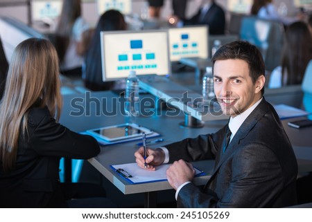 Young handsome business man is looking at the camera during presentation in modern conference hall.