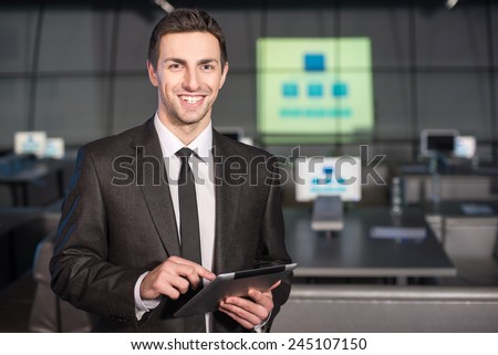 Portrait of a handsome young man with tablet is standing in the background of the modern conference hall.