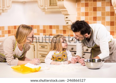 Happy parents and their young daughter are cooking, baking cakes in home kitchen.