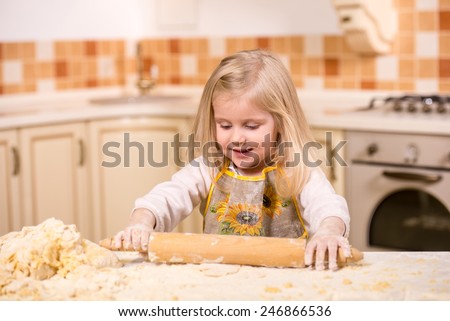 Little girl using a rolling pin to knead dough in the kitchen.