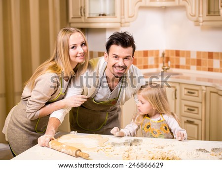 Happy parents and their young daughter are cooking, baking cakes in home kitchen.