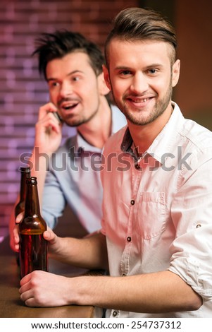 Two young handsome friends in a pub with bottle of beer are spending time together.