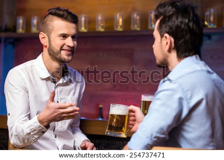 Two cheerful young men in shirt with beer while sitting together at the bar counter.