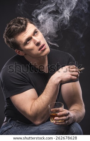 Young man is smoking a cigarette and is drinking whiskey over dark background.