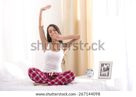 Beautiful happy young woman waking up in the morning and stretching in bed at home.
