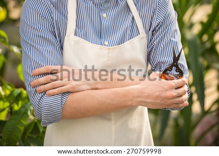 Close-up. Male florist holding hands crossed with secateurs in flowers shop.