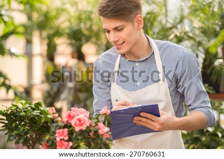Young handsome male florist watching on flowers and making notes.